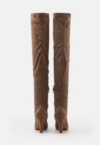 Botas de ante marrón hasta la rodilla con un diseño ajustado, tacón afilado y cierres de cremallera en los costados para ponerlas y quitarlas fácilmente. Textura suave en todo el calzado.