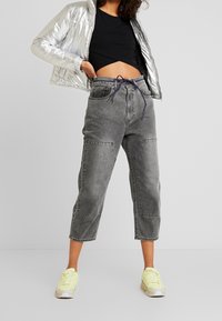 Sølv pufferjakke, sort cropped top, grå denimbukser med to sidelommer og neongule sneakers. Moderne afslappet pasform.