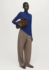 Modra rebrasta pulover z visokim ovratnikom, kombiniran z ohlapnimi bež hlačami. Model drži rjavo tkaninsko ročno torbico; stoji na nevtralni podlagi.