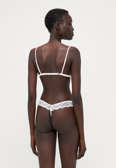 Set di lingerie bianca in pizzo con bralette a spalline sottili e slip coordinato con bordi ondulati, che mettono in mostra delicati motivi.