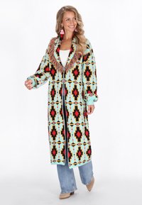 Cappotto lungo con una base turchese e motivi geometrici in rosso, nero e giallo. Presenta dettagli frangiati attorno al collo e una consistenza morbida.