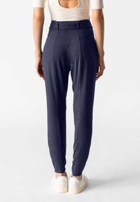 Marina smala byxor med hög midja, tillverkade av mjukt tyg. Elastiska mudd vid ankle; bärs med vita sneakers.