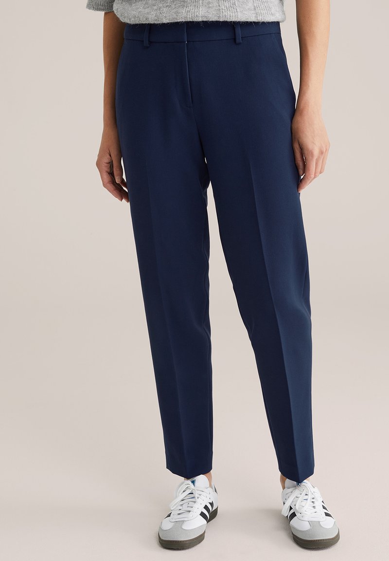 Pantalones de corte entallado en azul marino, fabricados en una tela suave, con un ajuste slim y piernas rectas, combinados con zapatillas blancas y grises.