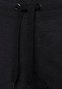 Zwarte joggingbroek met een platte tailleband en trekkoorddetails, gemaakt van een tekstuurstof en met metalen oogjes voor het trekkoord.