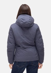 Giacca a piumino grigia, con cappuccio, trama trapuntata e silhouette aderente. Abbinata a jeans in denim scuro.