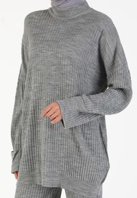 Grauer gerippter Strickpullover mit langen Ärmeln, hohem Kragen und lockerer Passform; verfügt über strukturierte vertikale Streifen und abgesenkte Schultern.