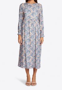 Vestido de manga larga con estampado floral en colores pastel. Escote redondo, cintura fruncida, llega hasta la mitad de la pantorrilla. Se lleva con sandalias nude.