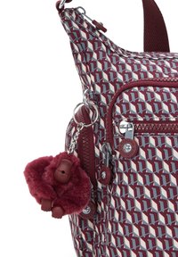 Zaino con motivo geometrico bordeaux, zip bordeaux e un portachiavi a forma di scimmia pelosa bordeaux attaccato a un anello di metallo.