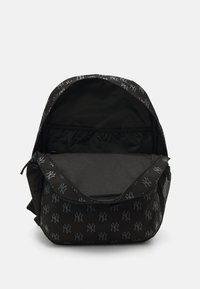 Sac à dos noir avec motif logo NY gris, fermeture éclair, intérieur spacieux, matériau en tissu, et poche en mesh sur le côté pour un rangement supplémentaire.