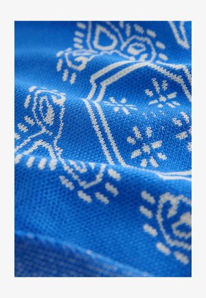 Niebieska dzianina z białym, misternym wzorem zawierającym motywy geometryczne i kwiatowe, prezentująca teksturowaną powierzchnię i cieniowanie.