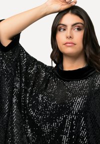 Poncho negro con lentejuelas y un suave cuello de terciopelo. Presenta un diseño suelto y fluido, y una textura brillante gracias a las lentejuelas densamente empaquetadas.