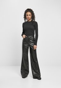 Haut noir à manches longues avec un col texturé, associé à un pantalon en cuir noir large à taille haute. Fini lisse et brillant sur le pantalon.