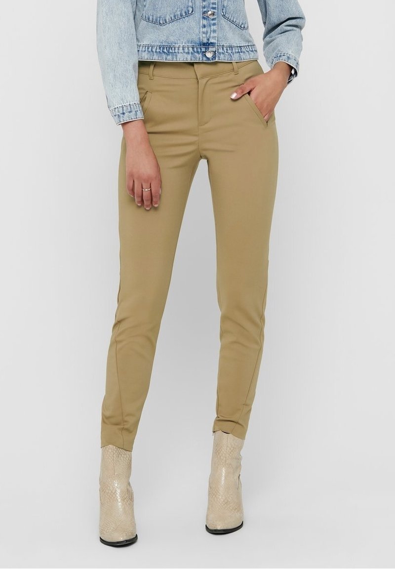 Bruna, figursydda byxor med sidofickor, som har en mjuk textur och en tapered design vid anklarna. Matchas med en ljus jeansjacka.