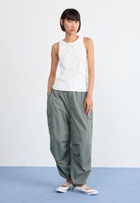 Un maiou alb cu dungi, asociat cu pantaloni cargo largi, de culoare verde măsliniu, care au buzunare laterale și manșete elasticate. Purtați cu pantofi albi slip-on.