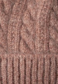 Tissu en tricot de couleur rose doux avec un motif en câble épais et une texture côtelée. Les fibres semblent duveteuses, renforçant la chaleur et le confort.