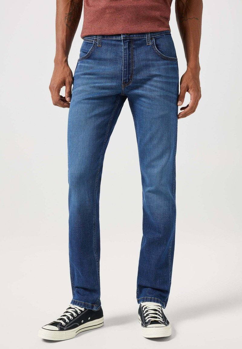 Ciemnoniebieskie dżinsy z prostymi nogawkami, z przednimi kieszeniami, kontrastowym przeszyciem i zużytym wykończeniem. W zestawie z czarnymi sneakersami.