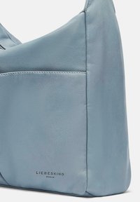 Borsa a tracolla in pelle azzurro chiaro con una texture morbida, forma curva e dettagli di cucitura discreti. Presenta un logo in rilievo sul fronte.