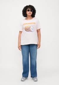 Light pink t-shirt featuring a coconut graphic and the word "Coconut" in orange. Paired with blue denim jeans and silver sneakers.