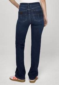 Temno moder denim jeans z ravnim krojem nogavic. Imajo dva zadnja žepa, visok pas in kontrastne šive.