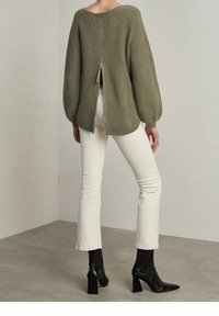 Oliivinvihreä neulepusero, jossa on takana vetoketju, ribbitetty pinta ja pussihihat, yhdistetty valkoisiin istuviin farkkuihin ja mustiin korkokenkiin.