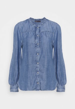 Blusa de mezclilla azul con mangas largas, cuello con volantes y cierre frontal con botones decorado con volantes.