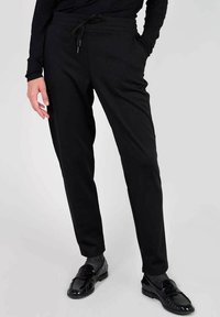 Svarta joggingbyxor i elastisk tyg med dragsko i midjan, smal passform och sidofickor. Släta textur med minimalistisk design.