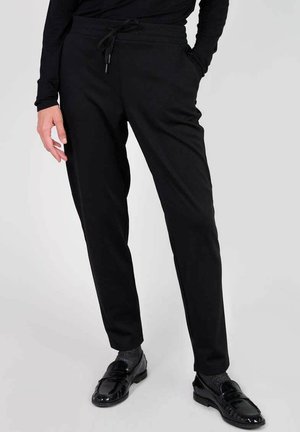 Black jogger pants made of elastic fabric, featuring a drawstring waistband, slim fit, and side pockets. Smooth texture with minimal design.