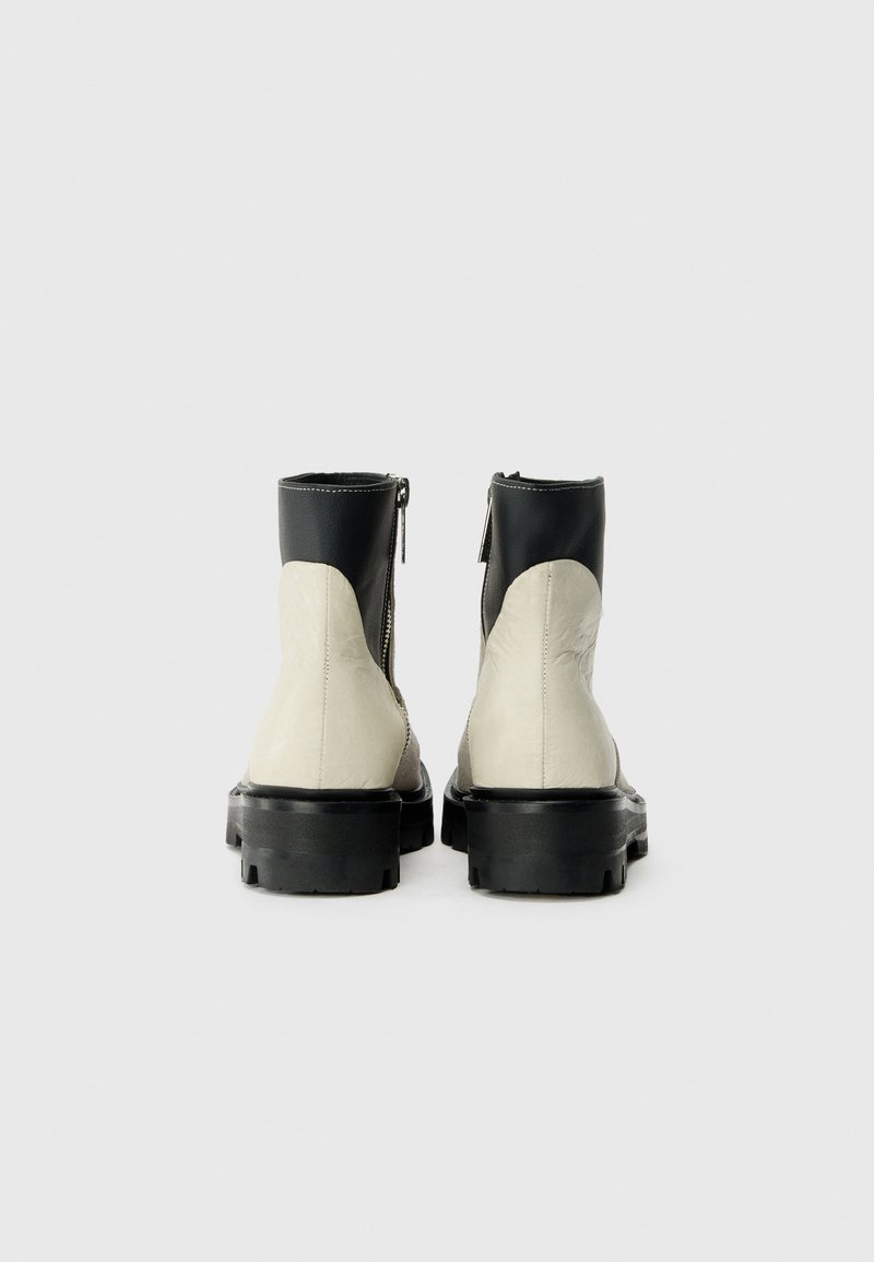 Schwarze Leder-Ankle-Boots mit einem cremefarbenen Kunstleder-Unterschuh, seitlichem Reißverschluss und robuster schwarzer Sohle. Glatte Textur und minimalistisches Design.