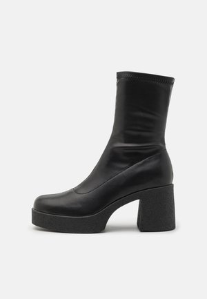 Bottine en cuir noir avec un talon bloc haut et une plateforme texturée. Présente une finition lisse et des coutures décoratives le long des côtés.