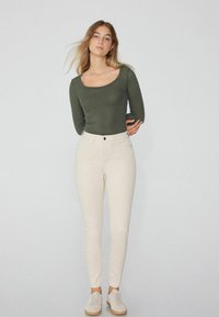 Top de manga larga en verde oliva con textura de canalé, jeans crema de cintura alta y zapatillas claras. Ajuste slim, escote redondo y textura sutil en la tela.
