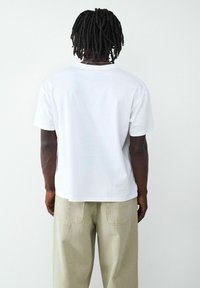 Biała bawełniana koszulka z krótkimi rękawami i prostym krojem, w zestawie z wysokimi spodniami w jasnym odcieniu khaki, które mają tylne kieszenie.