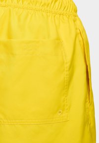 Shorts jaunes avec une taille élastique, de grandes poches latérales et une poche patch au dos avec des détails de couture visibles.