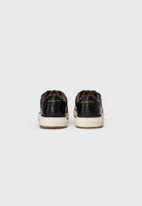 Fekete bőrsneaker fehér gumitalppal, alacsony kivágással és sárga logórészlet a saroknál. Texturált hátsó panel.
