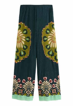 Pantalon à jambes larges vert foncé avec de grands motifs floraux en olive, crème, bleu et rose sur les jambes et l’ourlet.