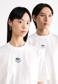 Hvite bomull T-skjorter med rund hals, med en marineblå Lacoste-logo på brystet. Enkel og klassisk design med korte ermer.
