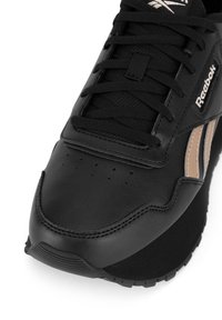 Sneaker nero in pelle con finitura testurizzata, chiusura con lacci e marchio Reebok. Strisce beige accentuano il lato.