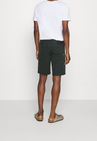 Ciemnozielone szorty wykonane z tkaniny, o klasycznym kroju, z tylnymi kieszeniami i subtelnym logo nad prawą kieszenią.