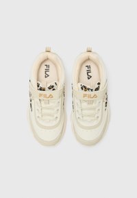 Cremefarbene Sneakers mit einer glatten, lederähnlichen Oberfläche, die ein schwarz-beiges Leopardenmuster entlang der Seite und einen Klettverschluss aufweisen.