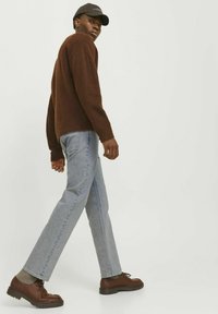 Suéter marrón texturizado, jeans de mezclilla azul claro y zapatos marrones de cordones. El modelo también lleva una gorra negra. Enfóquese en el diseño de un atuendo casual.