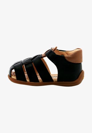 Sandal de cuero negro con diseño de punta abierta, múltiples tiras cruzadas y un talón trasero en color marrón. Suela de goma flexible para mayor comodidad.