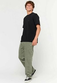 Czarny t-shirt z krótkim rękawem i subtelnym logo, zestawiony z jasnooliwkowymi spodniami sztruksowymi oraz czarnymi trampkami z białymi akcentami.