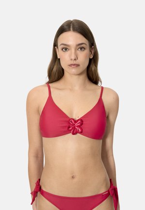 Mujer con bikini rojo de dos piezas, con detalle floral en el centro del top y lazos atados a los lados del pantalón, posando frente a un fondo liso.