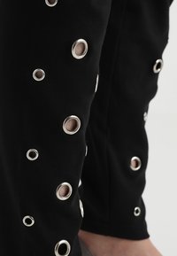 Fekete nadrág ezüst szemes díszítéssel a lábak mentén, sima textúrával és testre szabott kialakítással. Különböző laza stílusokhoz alkalmas.