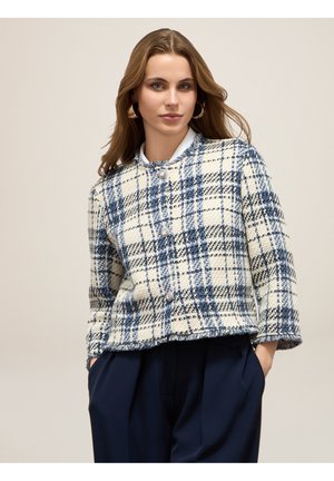 Veste à carreaux blanche et bleue avec une finition texturée, encolure ronde et deux boutons. L'ourlet est légèrement effiloché pour une touche de détail supplémentaire.