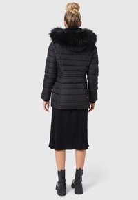 Schwarze Steppjacke mit einer Kapuze aus Kunstfell, horizontalen Nähten und gerippten Akzenten, kombiniert mit einem schwarzen gerippten Rock und Stiefeletten.