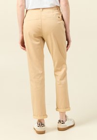 Beige bomullsbyxor med rak bendesign, uppvikta fållar och två bakfickor. Matchas med vita sneakers med leopardmönstrade detaljer.