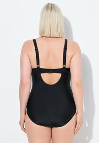 Costume da bagno intero nero con spalline regolabili, scollatura posteriore profonda e texture liscia e opaca. Nessun motivo visibile o hardware distintivo.