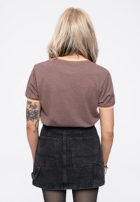 Brown short-sleeve t-shirt with orange trim, paired with a black denim skirt featuring two back pockets, viewed from the back.