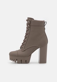 Bottes à plateforme épaisses couleur taupe, fabriquées en matériau lisse. Elles présentent un bout arrondi, un talon bloc haut et un laçage prononcé avec des détails de couture.