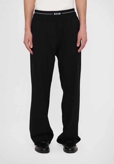 Pantalons larges noirs en tissu lisse, dotés d'une taille élastique avec un logo "MSGM" blanc et d'un cordon de serrage pour un ajustement réglable.